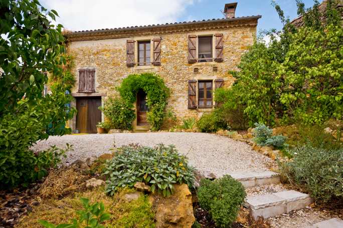 A traditional stone house with wooden shutters and surrounded by lush green foliage