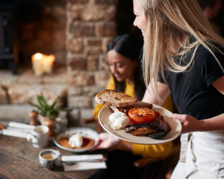 A fluffy golden retriever puppy sits calmly in the middle of a sunlit field filled with blooming white daisies.