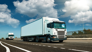 White semi‑truck driving on a highway under a bright sun with blue sky and clouds