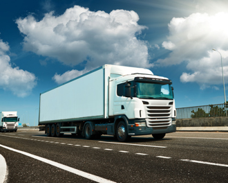 White semi‑truck driving on a highway under a bright sun with blue sky and clouds