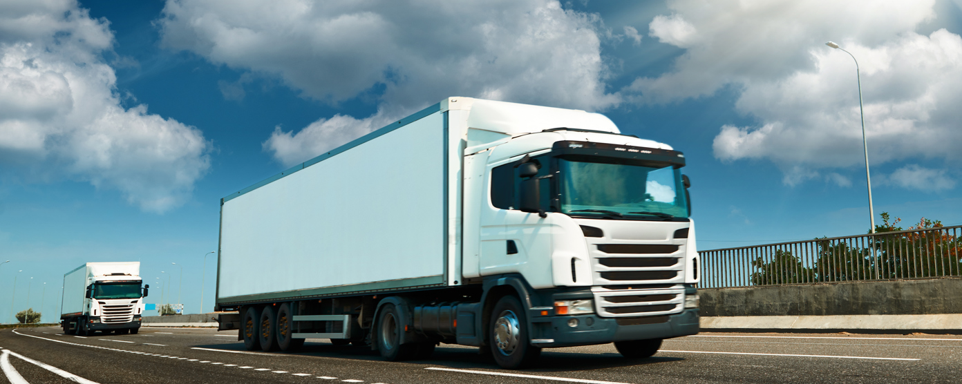 White semi‑truck driving on a highway under a bright sun with blue sky and clouds
