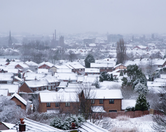 A wide view of a suburban neighborhood blanketed in snow, with rows of houses topped with white rooftops.