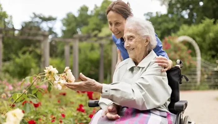 Carer supporting an elderly woman in a wheelchair as they enjoy roses together in a garden