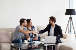 A couple shakes hands with a professional in a home setting, likely a real estate agent or financial advisor