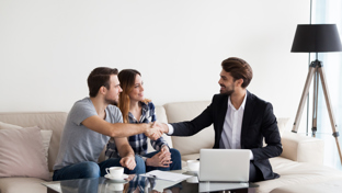 A couple shakes hands with a professional in a home setting, likely a real estate agent or financial advisor
