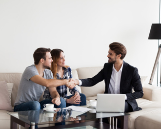 A couple shakes hands with a professional in a home setting, likely a real estate agent or financial advisor