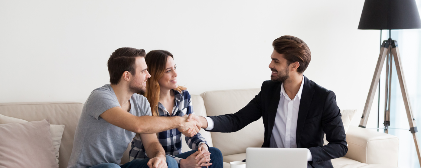 A couple shakes hands with a professional in a home setting, likely a real estate agent or financial advisor