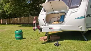 Open front locker of a touring caravan with a detached gas bottle on grass at a campsite