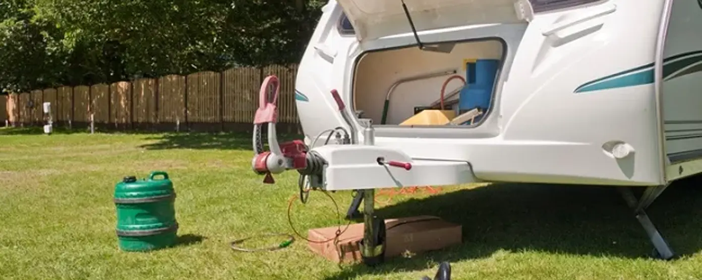 Open front locker of a touring caravan with a detached gas bottle on grass at a campsite
