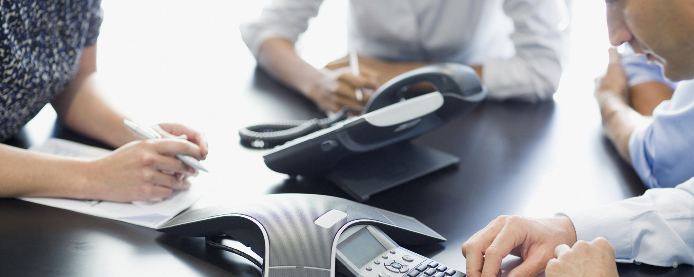 Three business professionals are seated around a conference table, writing notes while participating in a meeting.