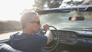 Man wearing sunglasses driving a classic convertible on a sunny day, viewed from the passenger seat