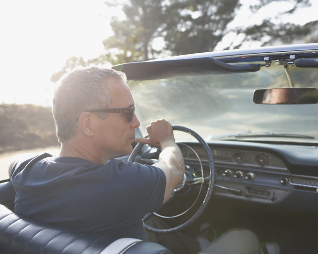Man wearing sunglasses driving a classic convertible on a sunny day, viewed from the passenger seat