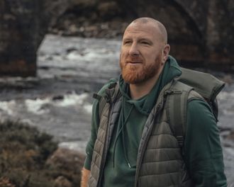 Man looking into the distance with a water and bridge behind in the background