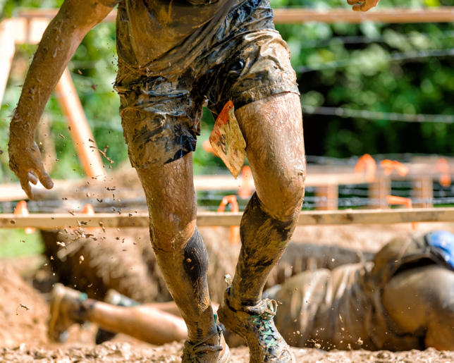 man rising out of barbwire mud pit in obstacle course