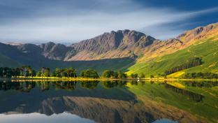 Mountain with calm waters reflecting the surrounding mountains and a line of trees along the shore under a clear sky