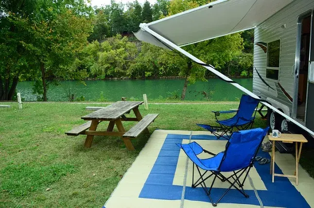 RV campsite with awning picnic table and two blue chairs beside a river