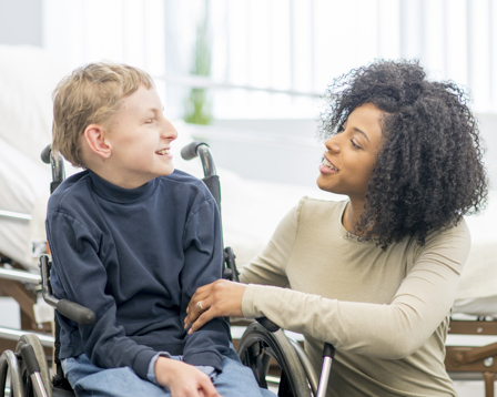 carer supporting a smiling child in a wheelchair at home