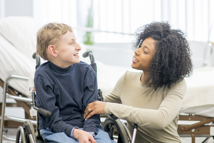 carer supporting a smiling child in a wheelchair at home