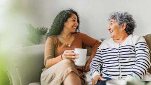 Two ladies it smiling on a sofa