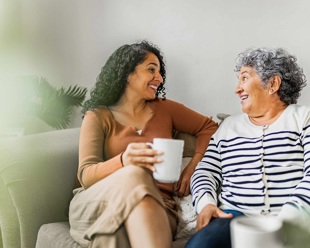 Two ladies it smiling on a sofa