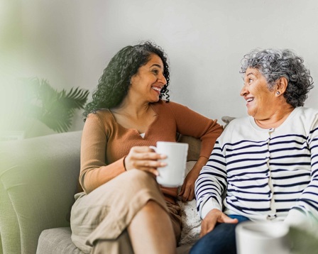 Two ladies it smiling on a sofa