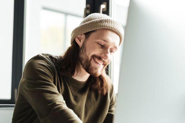 man wearing a hat smiling working on a laptop