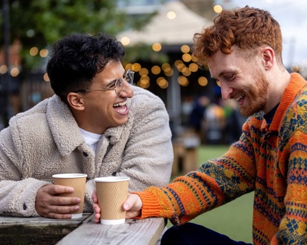 two men smiling over coffee in a park