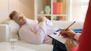 Therapist taking notes while a male patient lies on a couch during a counseling or therapy session