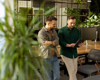 Two men standing in an office looking at a tablet