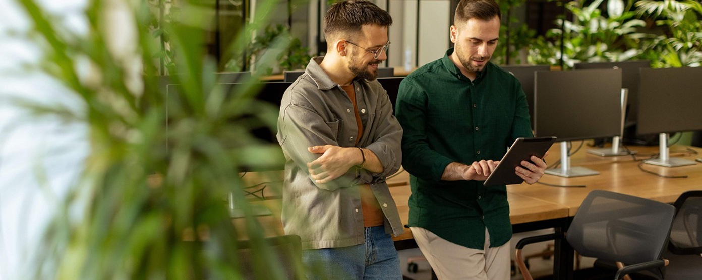 Two men standing in an office looking at a tablet