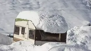 caravan buried in deep snow with a heavy layer on the roof.