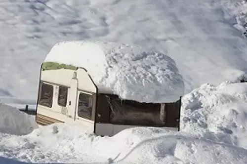 caravan buried in deep snow with a heavy layer on the roof.