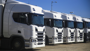 Line of white semi‑truck tractors parked in a logistics yard under a clear blue sky