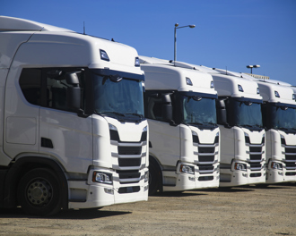 Line of white semi‑truck tractors parked in a logistics yard under a clear blue sky
