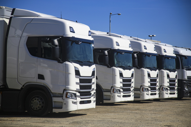 Line of white semi‑truck tractors parked in a logistics yard under a clear blue sky