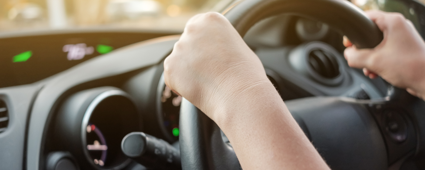 Hands gripping a steering wheel while driving a car in bright daylight.