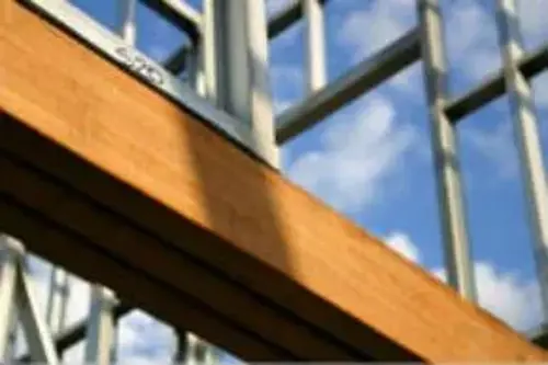 Close-up view of a steel frame construction with a wooden beam under a blue sky
