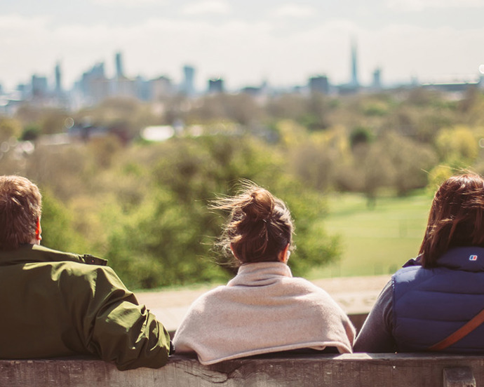 3 on bench, in a park with trees and busy towers along the skyline (Primrose Hill in North London, overlooking the city)