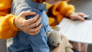 Close-up of an adult comforting a child holding a teddy bear while reviewing paperwork, with a gentle hand on the child’s shoulder