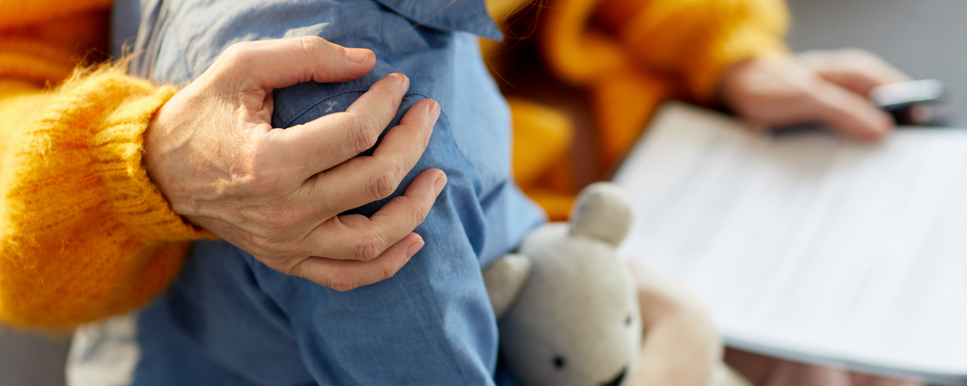 Close-up of an adult comforting a child holding a teddy bear while reviewing paperwork, with a gentle hand on the child’s shoulder