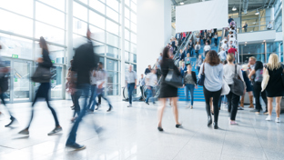 A lively scene in a spacious exhibition hall, showcasing people moving quickly, with some individuals appearing blurred