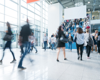 A lively scene in a spacious exhibition hall, showcasing people moving quickly, with some individuals appearing blurred