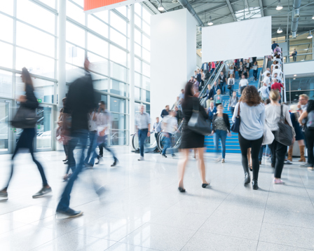 A lively scene in a spacious exhibition hall, showcasing people moving quickly, with some individuals appearing blurred