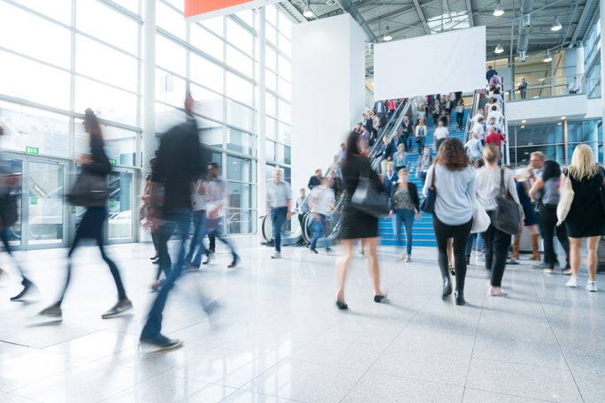 A lively scene in a spacious exhibition hall, showcasing people moving quickly, with some individuals appearing blurred