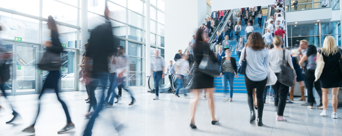 A lively scene in a spacious exhibition hall, showcasing people moving quickly, with some individuals appearing blurred