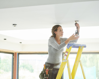 Woman installing a ceiling light while standing on a ladder.