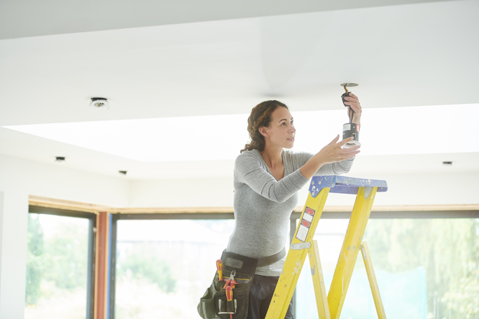 Woman installing a ceiling light while standing on a ladder.