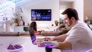 A man in a white t shirt sitting at his kitchen table using a laptop