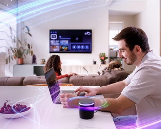 A man in a white t shirt sitting at his kitchen table using a laptop