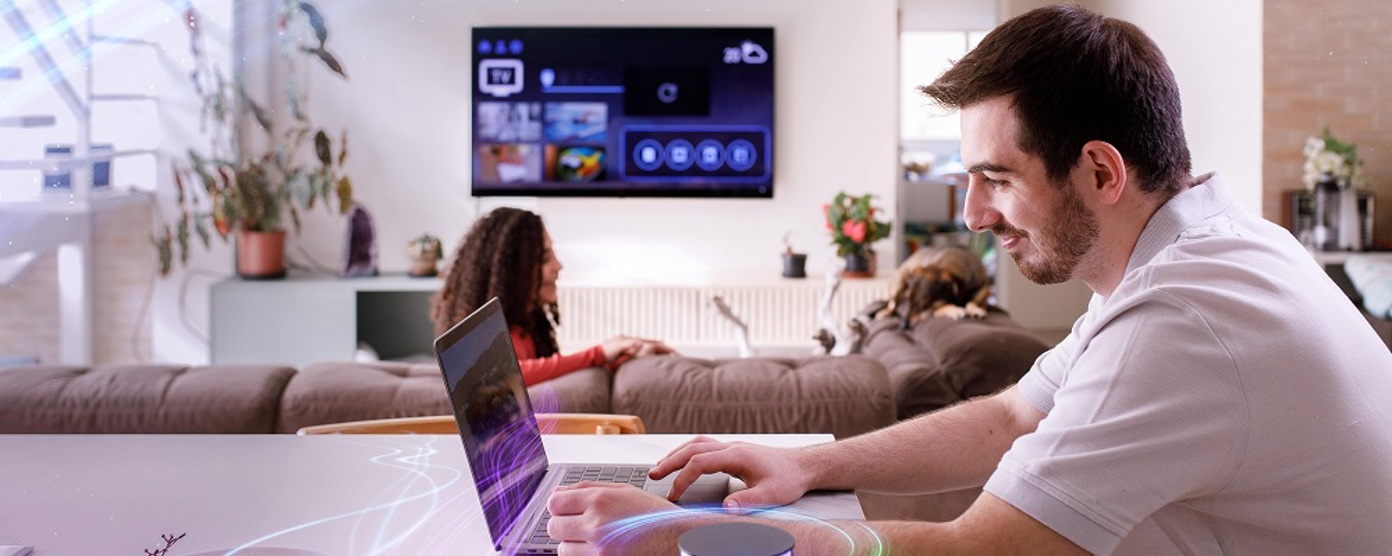 A man in a white t shirt sitting at his kitchen table using a laptop